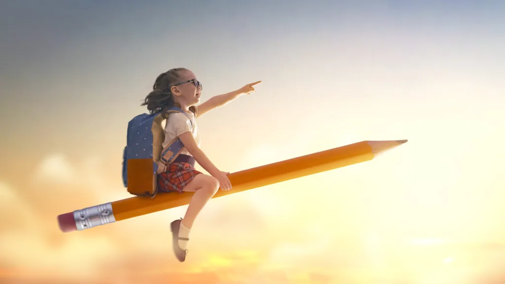 ランドセルを背負った女の子が、大きな鉛筆に乗って夕焼けの空を飛び、希望に満ちた表情で前方を指さしている