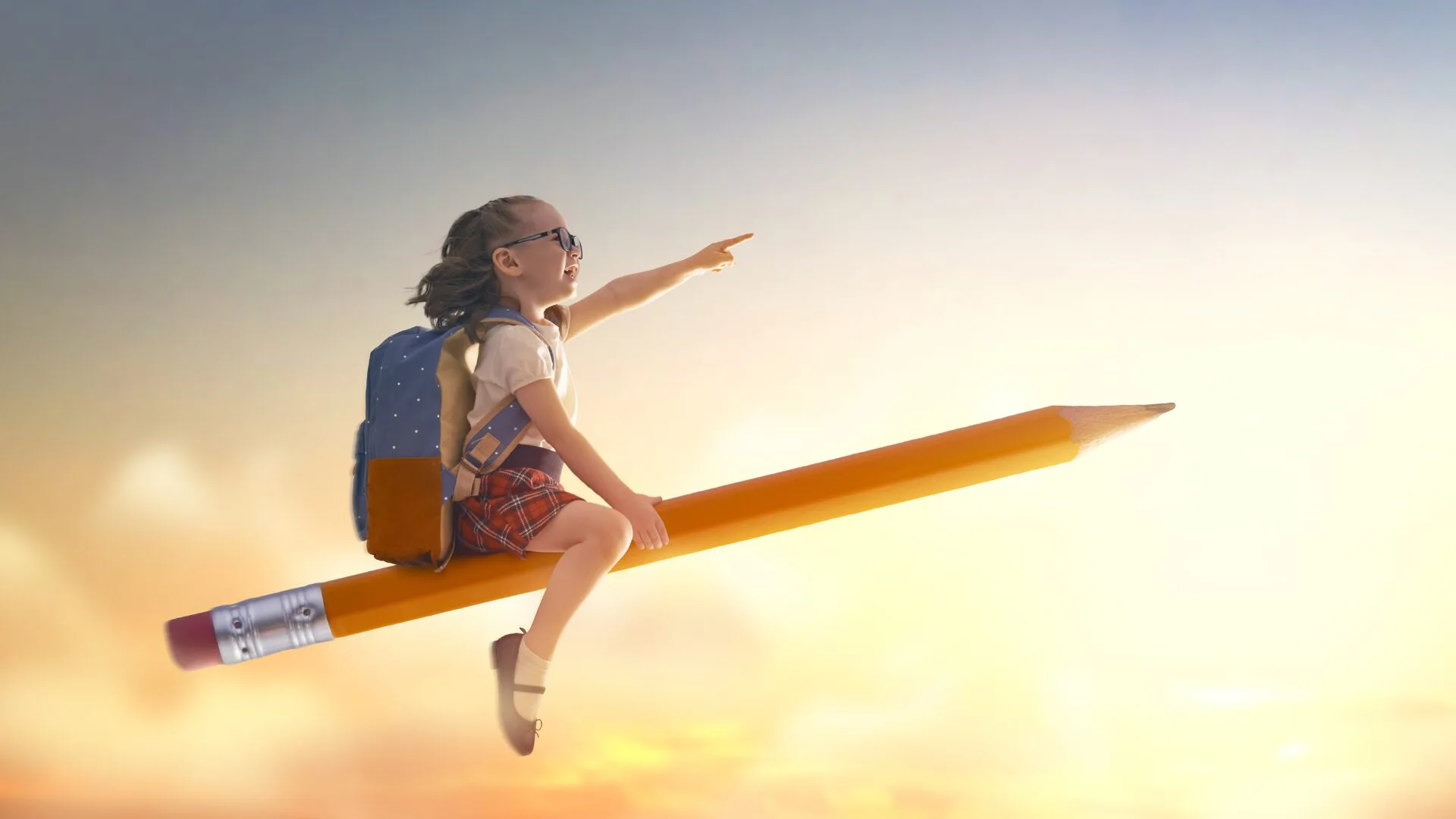 ランドセルを背負った女の子が、大きな鉛筆に乗って夕焼けの空を飛び、希望に満ちた表情で前方を指さしている