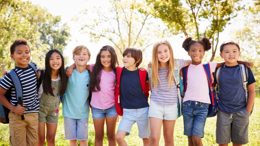 学童内で、多様な人種の子供たちが仲良く肩を組んで一列に並び、笑顔を見せている