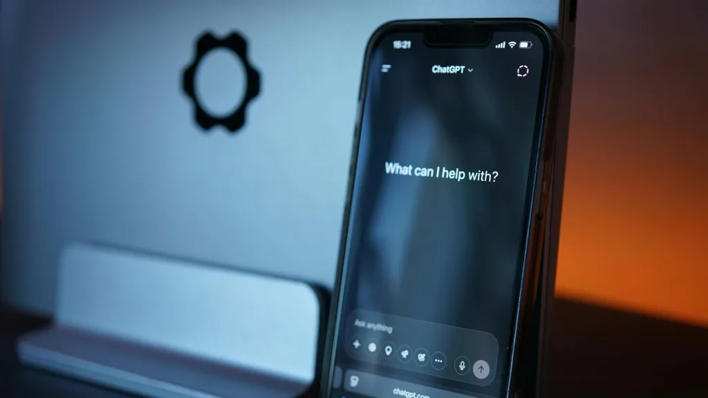 ノートパソコンの前に立てかけられたスマートフォンに、ChatGPTのアプリ画面が表示されている