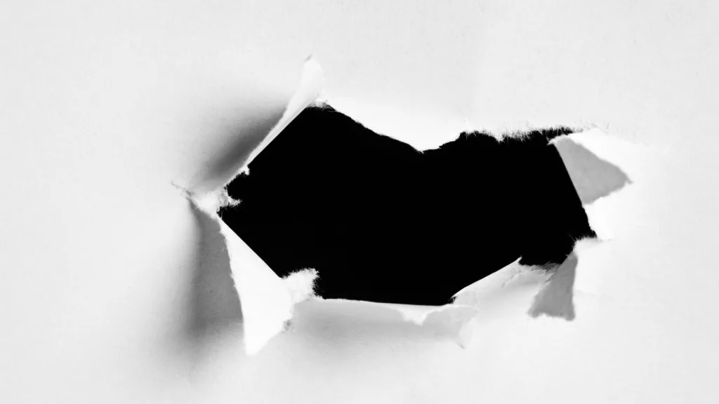 白い紙の中央が引き裂かれ、できた穴の向こう側に黒い背景が見えている
