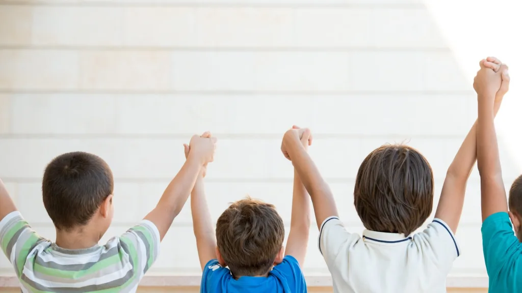 後ろ姿の4人の子供たちが、隣の子と手をつないで高く掲げている