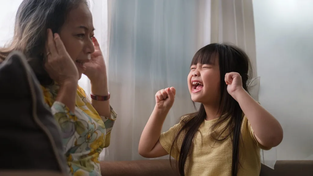 大きな口を開けて叫ぶ女の子と、その声に耳をふさぐ祖母
